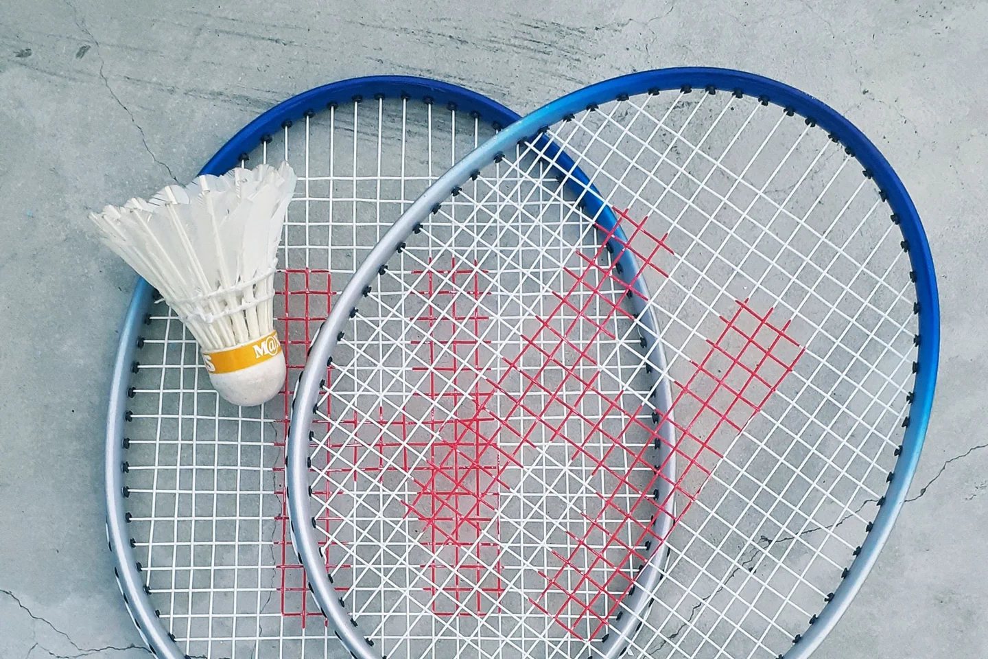 Two badminton rackets and a shuttlecock on a concrete surface