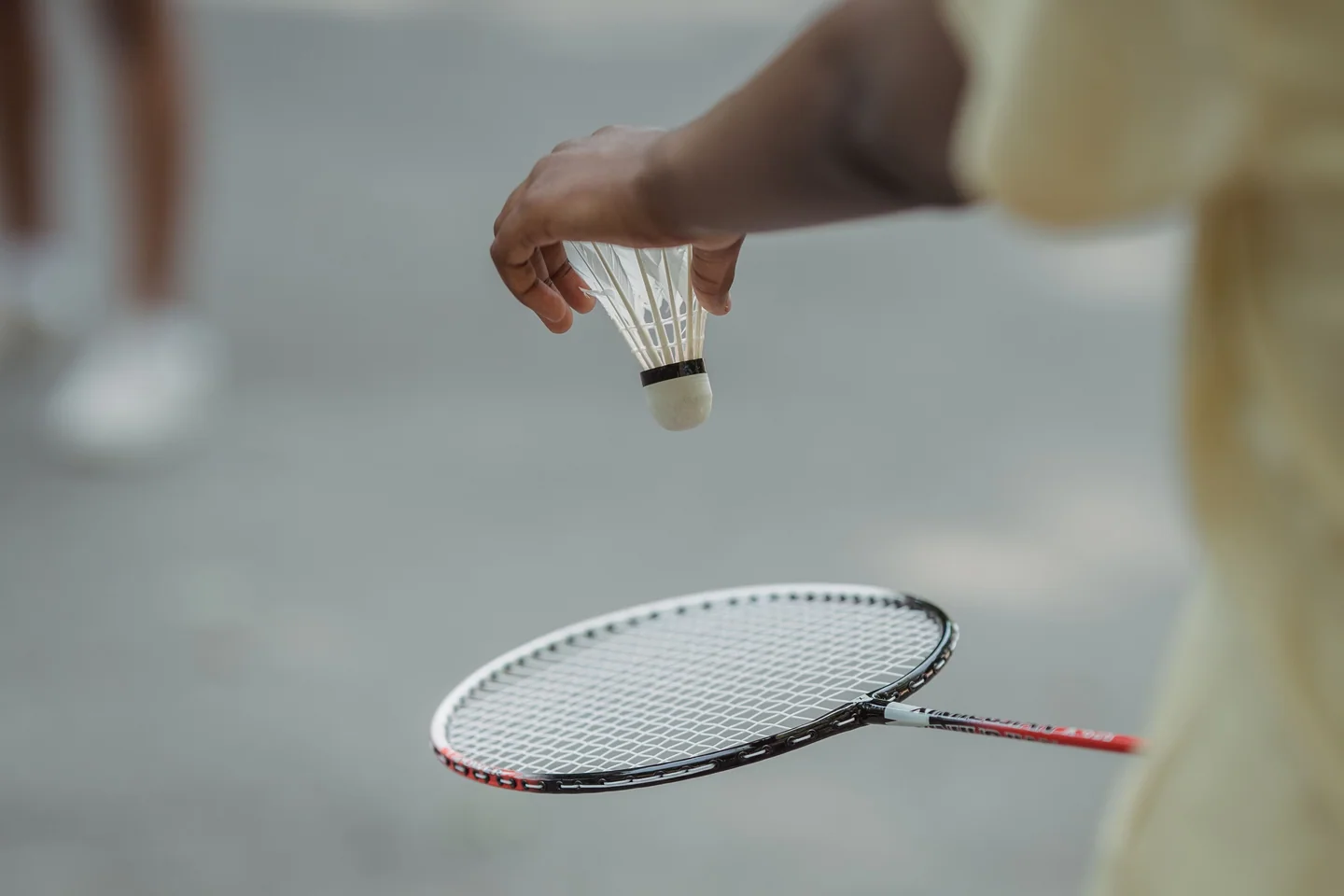A player holding a shuttlecock above a badminton racket before serving