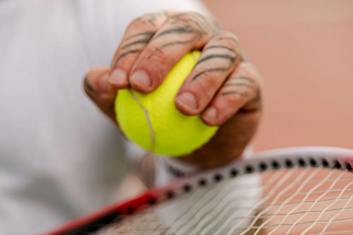 A player holding a tennis ball above the strings of a racket