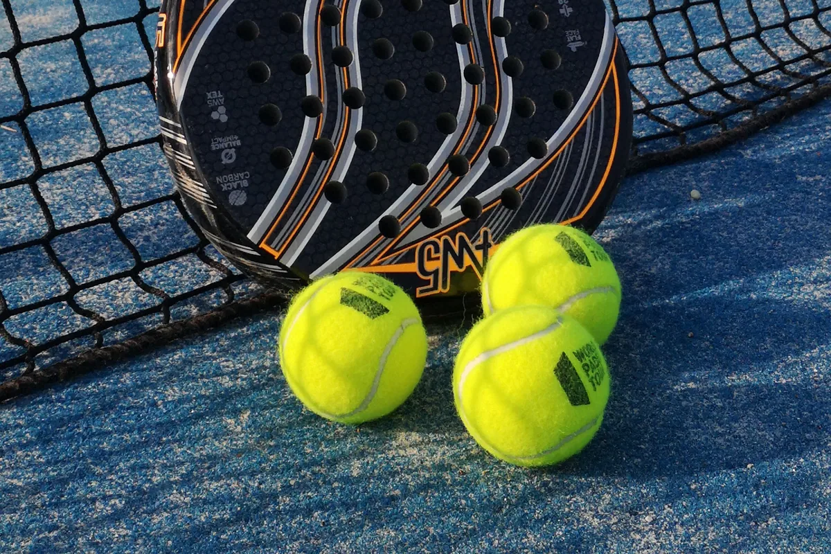 Padel racket and balls beside a net