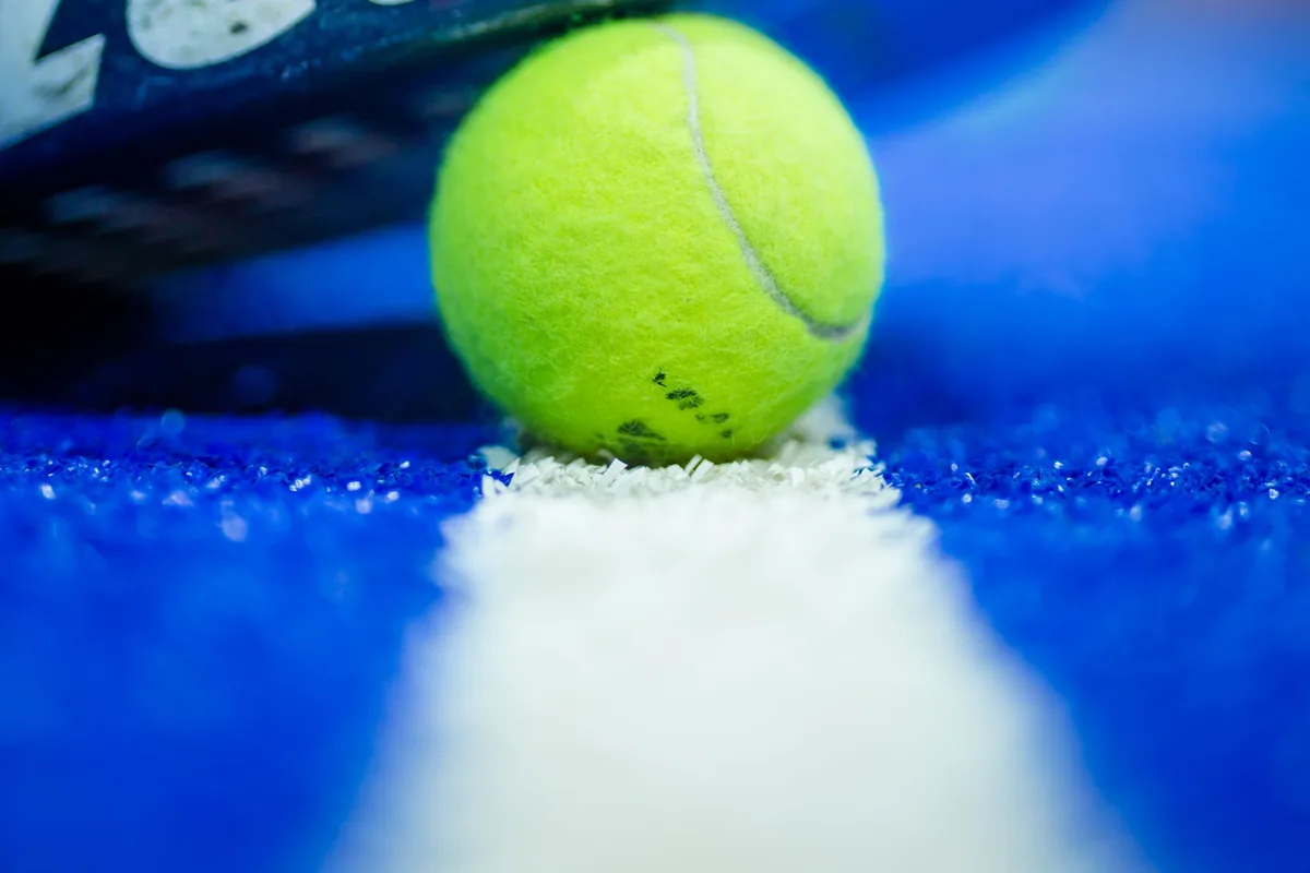 Padel racket edge and yellow ball on a blue court