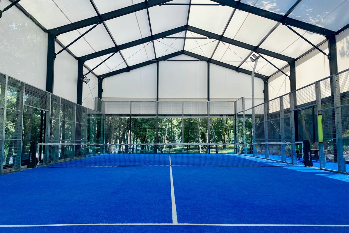 Blue indoor padel court surrounded by glass and metal fencing