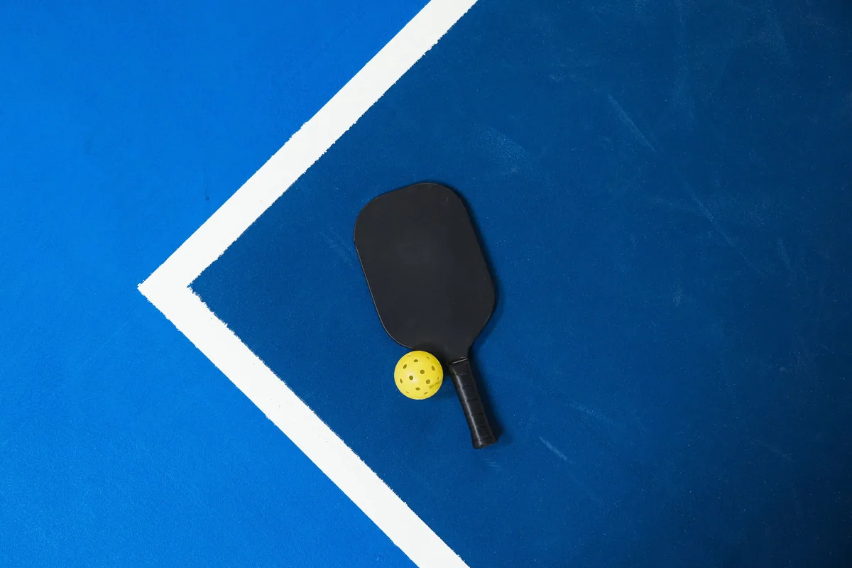 Yellow perforated ball and paddle beside white court lines