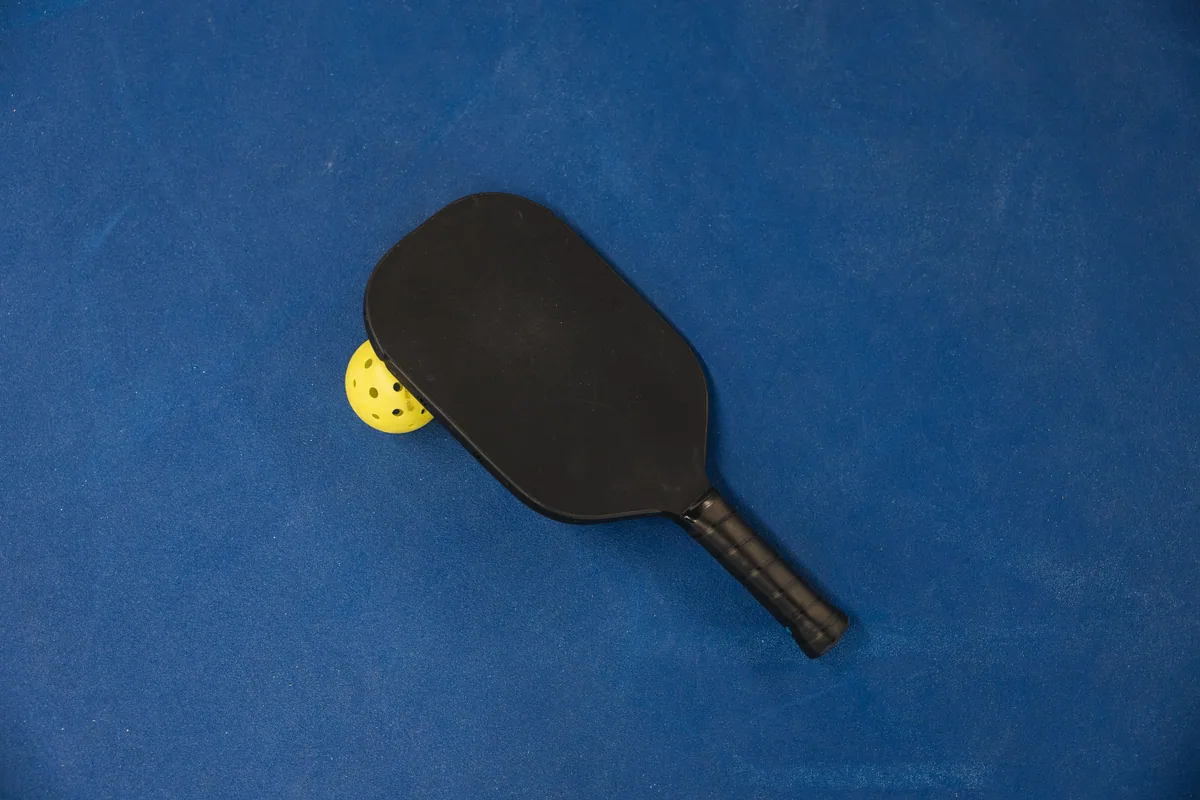 Black pickleball paddle and yellow ball on a blue court