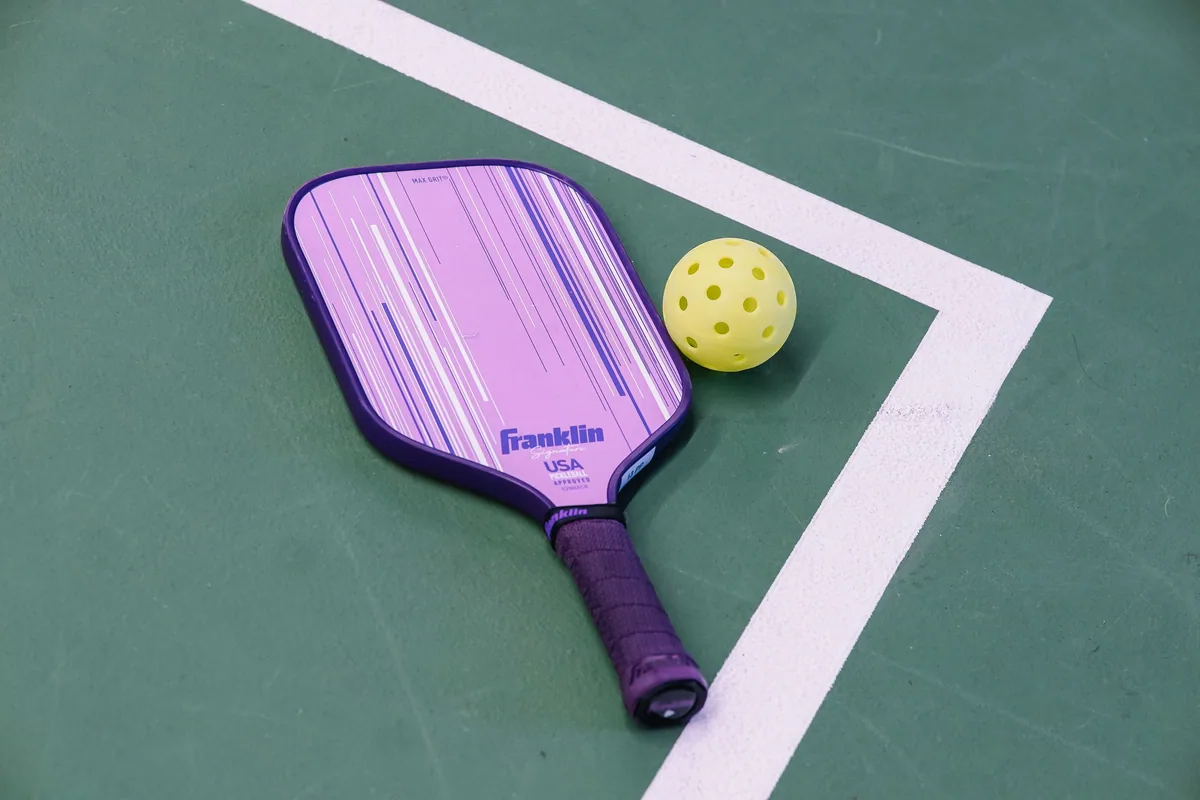 Purple pickleball paddle with wrapped handle beside a yellow ball