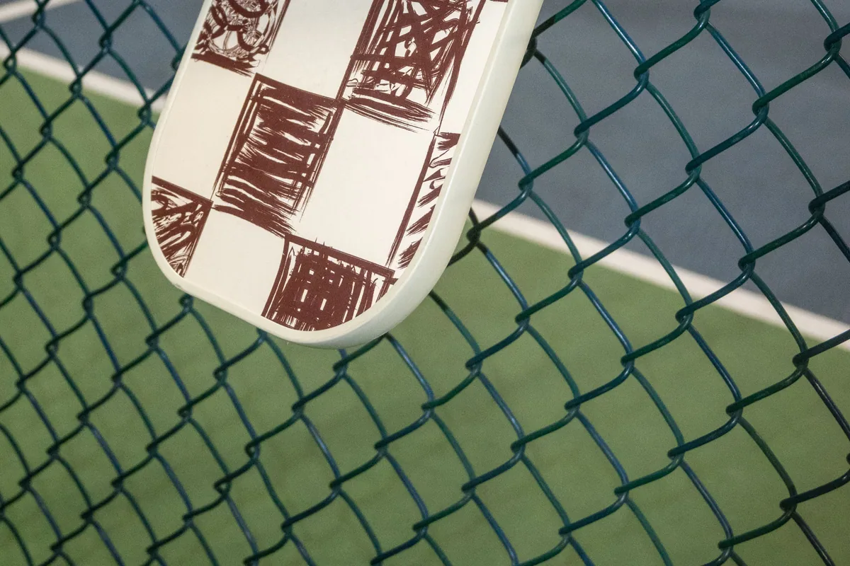 Checkered pickleball paddle hanging on a fence