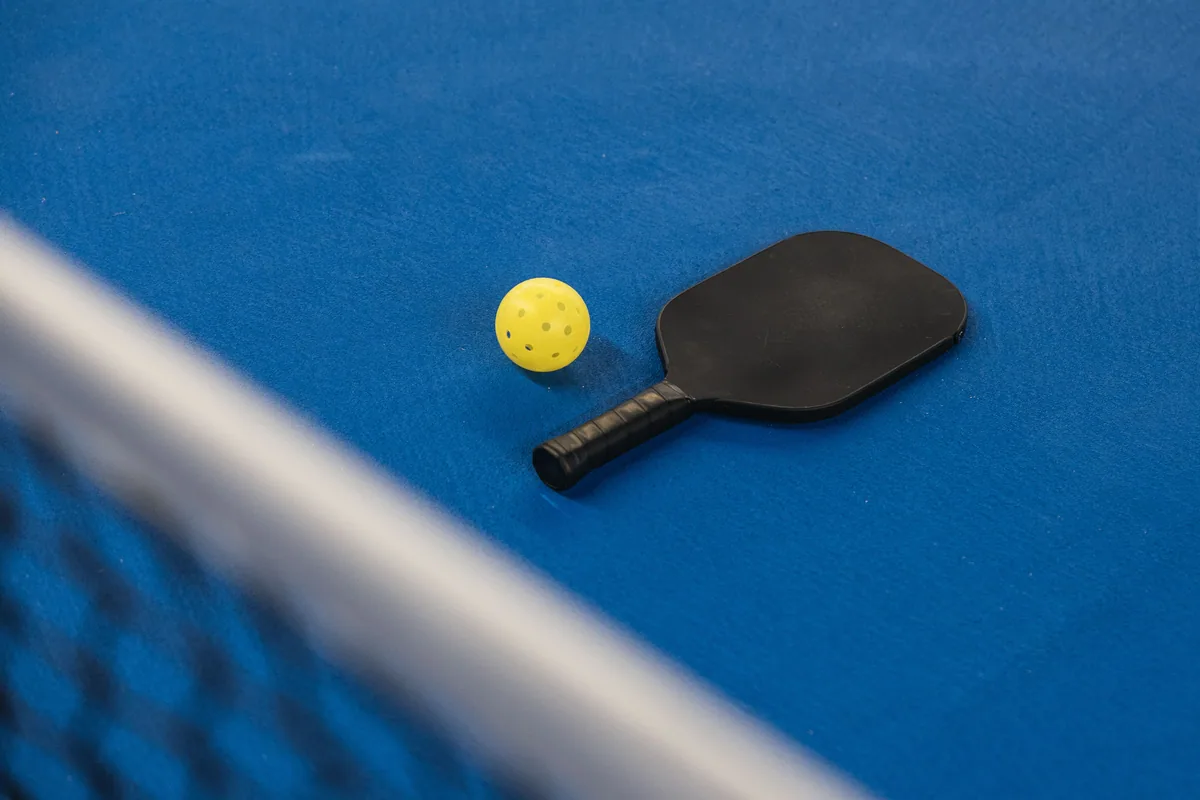 Pickleball paddle and perforated ball beside a net