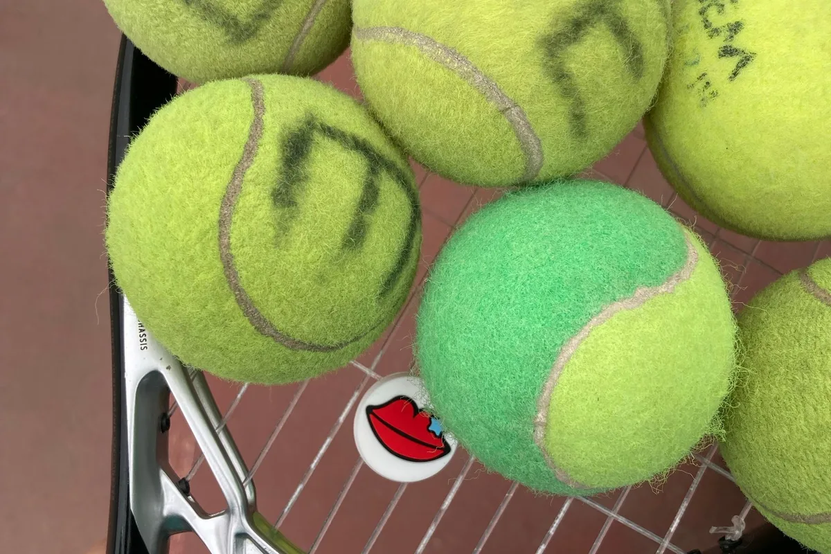 Tennis balls resting on racket strings