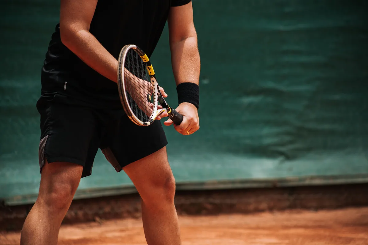 Hands holding a tennis racket on a clay court